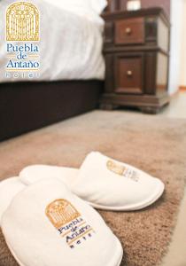 Dos zapatillas blancas sentadas en el suelo en una habitación de hotel en Hotel Puebla de Antaño, en Puebla