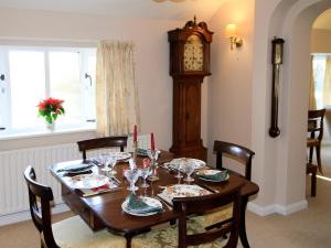 une table en bois avec des chaises et une horloge grand-père dans l'établissement Stable Cottage, à Lyminster