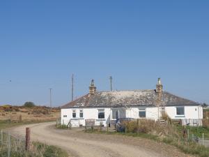 una casa bianca sul ciglio di una strada sterrata. di Kirklauchline Cottage a Portpatrick