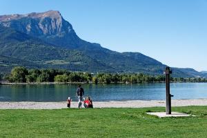 a man and two children standing on the shore of a lake at Studio à 200 mètres la plage du Plan d'eau in Embrun