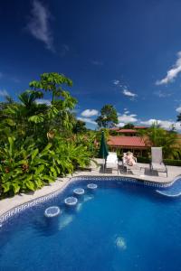 una piscina in un resort con due persone sedute su sedie di Arenal Volcano Inn a Fortuna