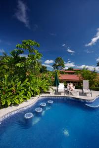 a pool at a resort with two people sitting in chairs at Arenal Volcano Inn in Fortuna