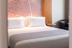 ein Schlafzimmer mit einem Bett mit weißen Kissen und einer Wand in der Unterkunft Abba Sants in Barcelona