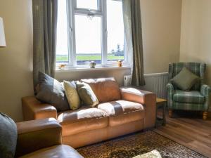 a living room with a leather couch and a window at Low Chibburn Farm Cottage in Hadston