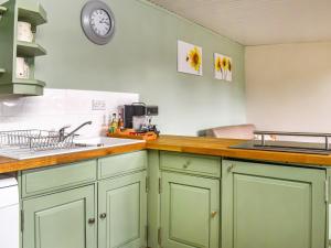 a kitchen with green cabinets and a clock on the wall at Newlyn Cottage in Pluckley