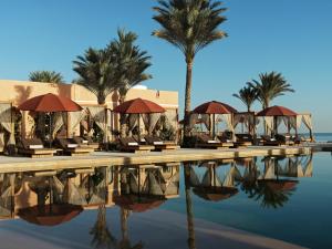 a resort pool with chairs and umbrellas and palm trees at The Chedi El Gouna in Hurghada