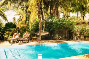 two people sitting in chairs next to a swimming pool at White Paradise Zanzibar in Pongwe