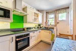 a kitchen with white cabinets and a green wall at Rose Cottage in Youlgreave