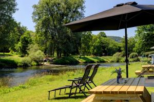 a picnic table with an umbrella and chairs next to a river at Lodge River wissel vr-ma camping Echternacherbrück in Echternacherbrück