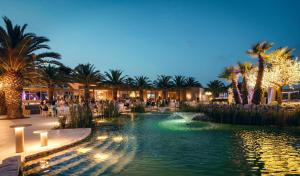 a pool in a resort with palm trees and lights at UNA HOTELS MH Matera in Matera