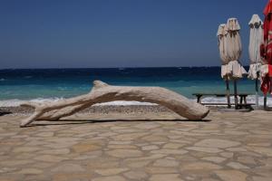 a piece of drift wood on a beach with umbrellas at Hotel Athena in Kokkari