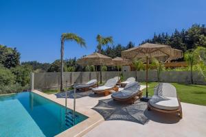 a swimming pool with chairs and umbrellas next to a swimming pool at Costas Luxury Villas - Costa's Villa in Koskinou