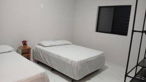 ein weißes Zimmer mit zwei Betten und einem Fenster in der Unterkunft Novíssima - Casa de Temporada a 09min do Thermas in Olímpia