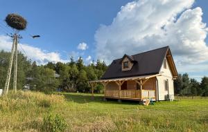 a small house with a black roof in a field at Bociani Zakątek nad jeziorem in Leszczewo