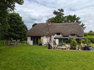 ein Haus mit einem Strohdach auf einem Grasfeld in der Unterkunft Far End Cottage in Fyfield