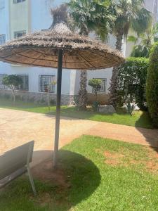 a straw umbrella sitting next to a bench at Appartement Cosy & Calme avec Piscine, Tamaris Dar Bouazza in Tamaris