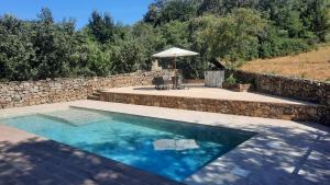 a swimming pool with a stone wall and an umbrella at La Torre de San Esteban in Bárcena de Ebro