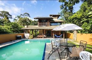 einen Pool mit Tisch und Stühlen und ein Haus in der Unterkunft Casa Juréia com piscina aquecida, a 350m da praia - Litoral Norte in São Sebastião