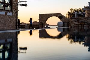 a woman walks by a swimming pool at sunset at Contaratos Beach Hotel in Naousa
