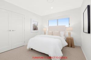 Un dormitorio blanco con una cama blanca y una ventana. en Serenity on the Green, en Sussex Inlet