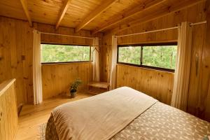 a bedroom with a bed in a wooden room with two windows at Loft Aneley in Algarrobo