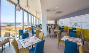 a restaurant with tables and chairs and large windows at Nicholas Color Hotel in Ayia Napa