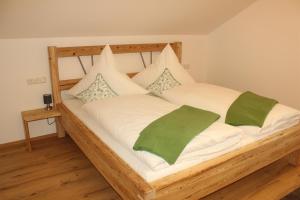 a wooden bed with white sheets and green pillows at Ferienwohnung Hutter in Fischen