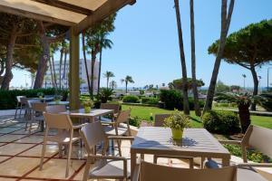a patio with tables and chairs and palm trees at Alua Illa de Menorca in S'Algar