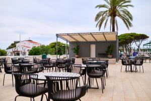 an outdoor patio with tables and chairs and palm trees at Alua Illa de Menorca in S'Algar