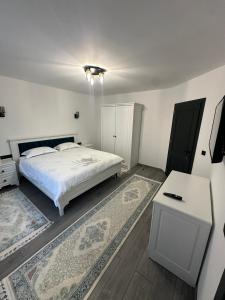 a white bedroom with a bed and a table and rug at Casa Sub Dumbravă in Bîrsana