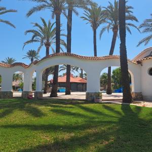 a white archway in a park with palm trees at Appartement El Palmar Denia in Denia