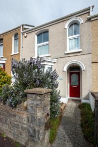 a house with a red door and a stone wall at Arfryn in The Mumbles
