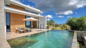 a swimming pool in front of a house with an umbrella at Villa Sambirano - avec piscine et vue mer - Nosy Be in Saint-Denis