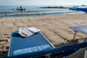 a blue bench on a beach with a boat in the water at Hotel Baia Del Capitano in Cefalù