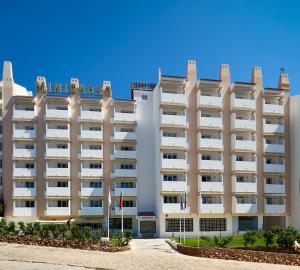 un gran edificio blanco con banderas delante en Cheerfulway Minichoro Apartamentos, en Albufeira