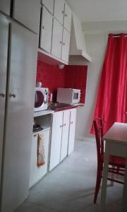 - une petite cuisine avec des placards blancs et un rideau rouge dans l'établissement L'essentiel, à Tours