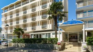 un edificio con una palma di fronte di Hotel Croce Di Malta a Lignano Sabbiadoro