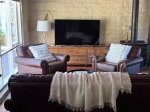 a living room with two leather chairs and a television at Elegant Country Living - The Homestead by Scotch Hill Truffle Farm in Neerim South