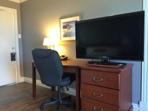 um quarto com uma secretária, uma televisão e uma cadeira em Hôtel Maison Blanche em New Carlisle