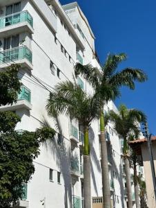 a tall white building with palm trees in front of it at Apartamento Cobertura vista ao mar churrasqueira Prainha Arraial do Cabo in Arraial do Cabo