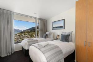 two beds in a hotel room with a large window at Central Sunset Charm in Queenstown