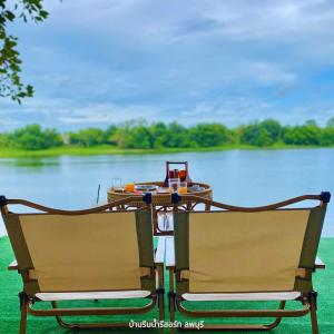 two chairs sitting in front of a table on a lake at Baanrimnam Resort Lopburi in Chai Badan
