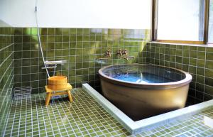 a tub in a green tiled bathroom with a window at 農ある暮らしの宿 古民家 天地 in Minamiizu