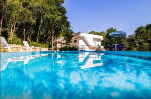 a large swimming pool with blue water in front of a house at Casa Bacarirá - Floresta com Yoga e Café da Manhã Vegano in Camburi