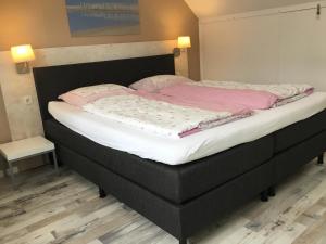 un grand lit avec un cadre noir et des draps roses dans l'établissement De Linden, à Egmond aan Zee