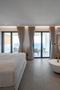a white bedroom with a large bed and a tub at The Royal Blue Andros in Batsi