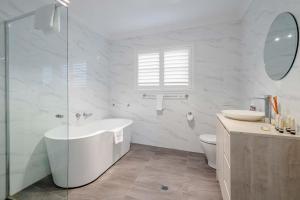 a white bathroom with a tub and a sink at Whisper on the Falls in Wentworth Falls