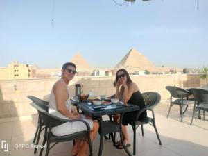 duas pessoas sentadas numa mesa com pirâmides ao fundo em Hassan Pyramids Hotel&Rooftop em Cairo