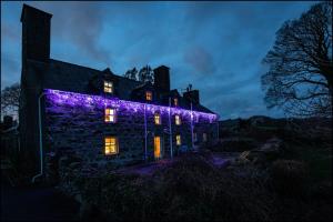an old stone house with purple lights on it at night at Betws Bach in Criccieth