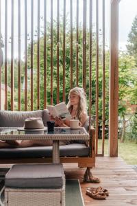 a woman sitting in a chair reading a book at Przystanek Roztocze- leśne SPA, Jacuzzi & sauna in Susiec